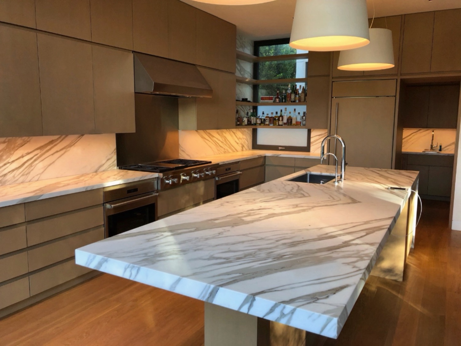 Calacatta marble island with a thick mitered edge in a warm contemporary kitchen, protected against acid etching